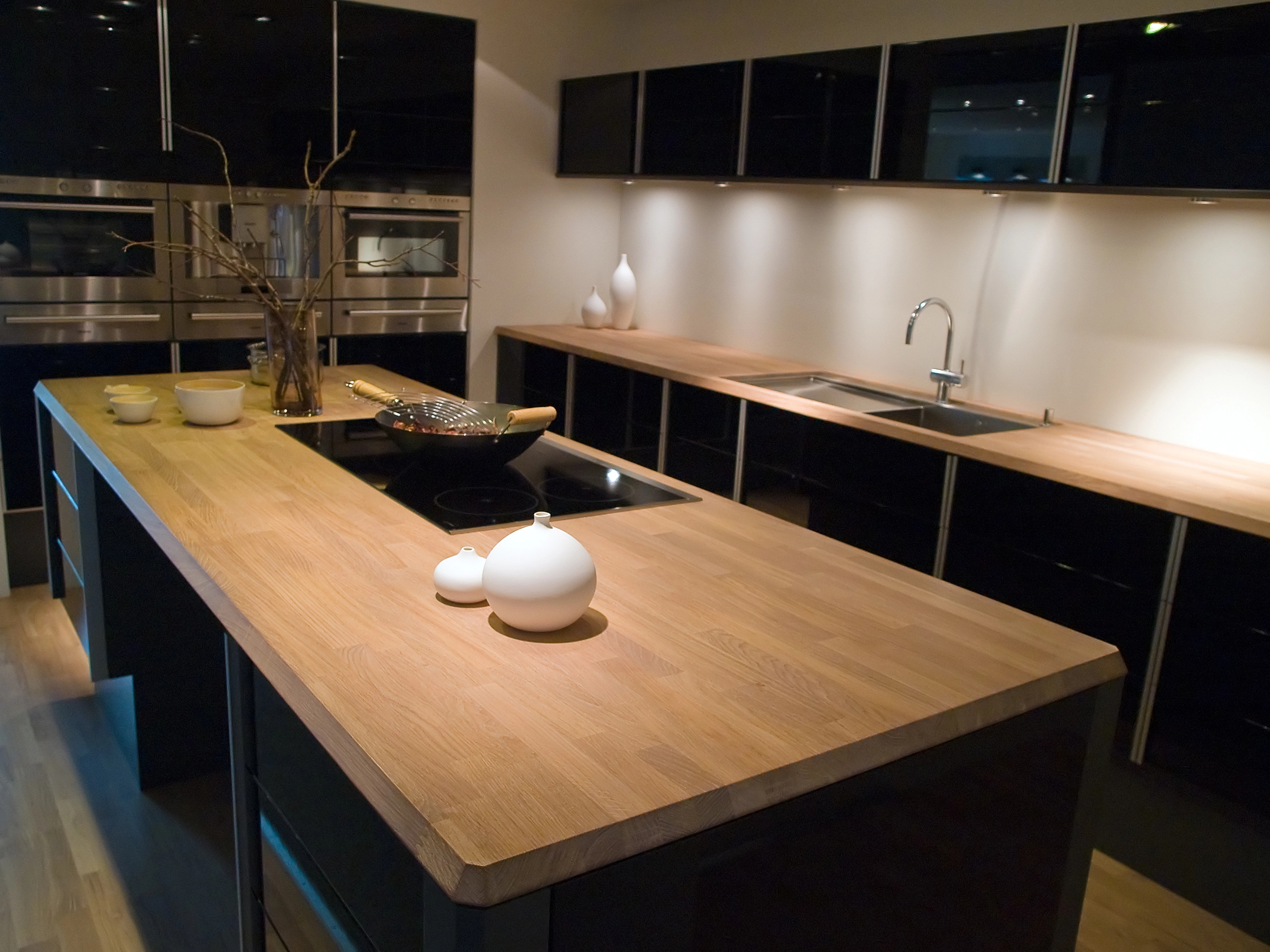 Modern kitchen with a wooden island countertop, built-in stove, minimalistic black cabinets, and decorative vases; warm lighting highlights the clean, contemporary atmosphere—ideal for seamless kitchen installations.